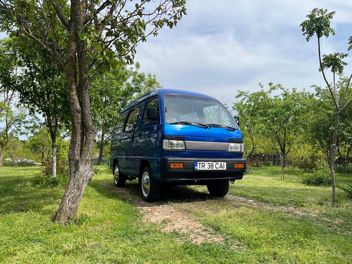 A blue 1997 Daewoo Damas parked in an orchard